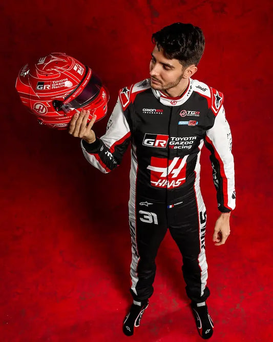 Person in racing suit holding a helmet against a red background