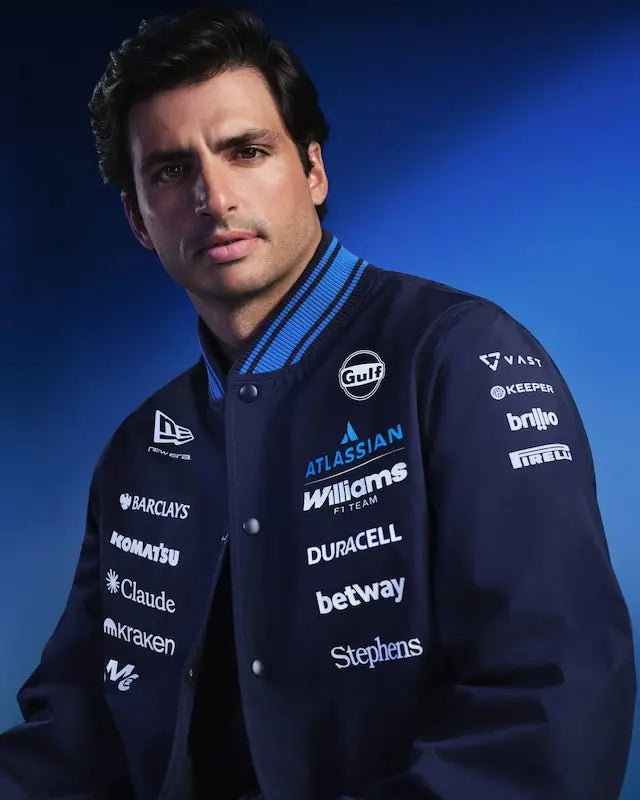 Man wearing a dark blue jacket with various sponsor logos against a blue background